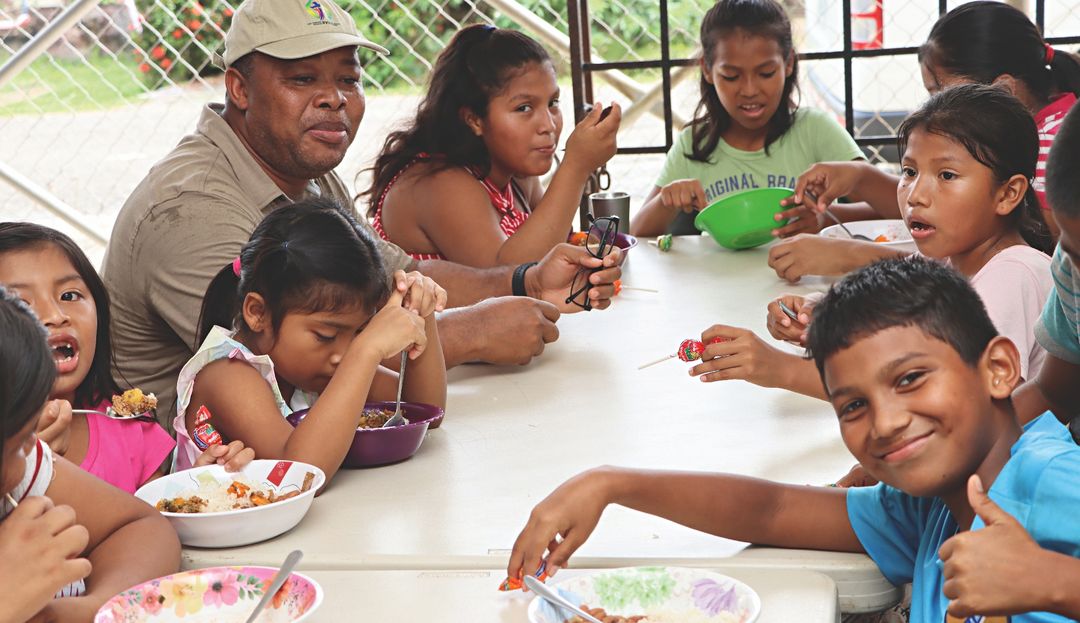 In der Steyler Kantine Santa Teresita bekommen Kinder ein kostenloses Frühstück und Mittagessen Mann und Kinder sitzen am Tisch und essen