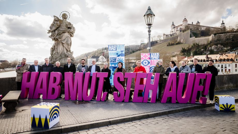 Menschen stehen in Würzburg um das Motto "Hab Mut, steh auf"