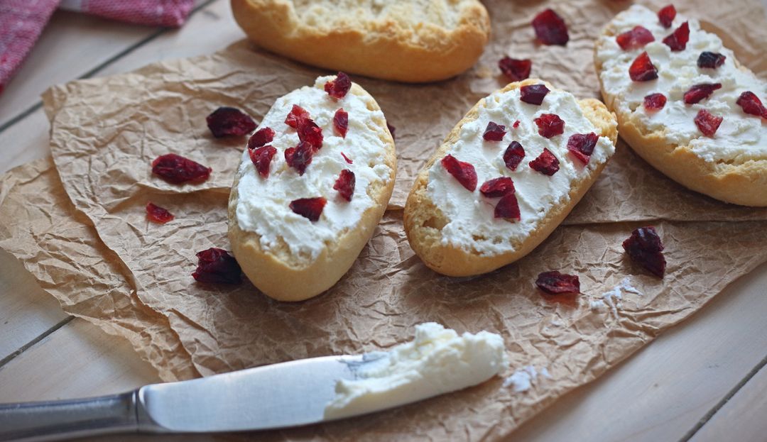 Messer mit Frischkäse, drei mit Cranberry-Aufstrich bestrichene Brotscheiben auf einem Papier