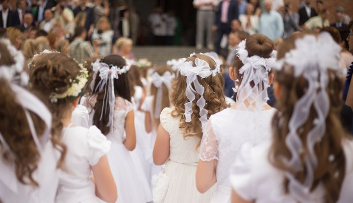 Wenn von der Kommunion oder Erstkommunion gesprochen wird, geht es um das Sakrament der Eucharistie Kommunionskinder stehen im weißen Kleid vor dem Kircheneingang