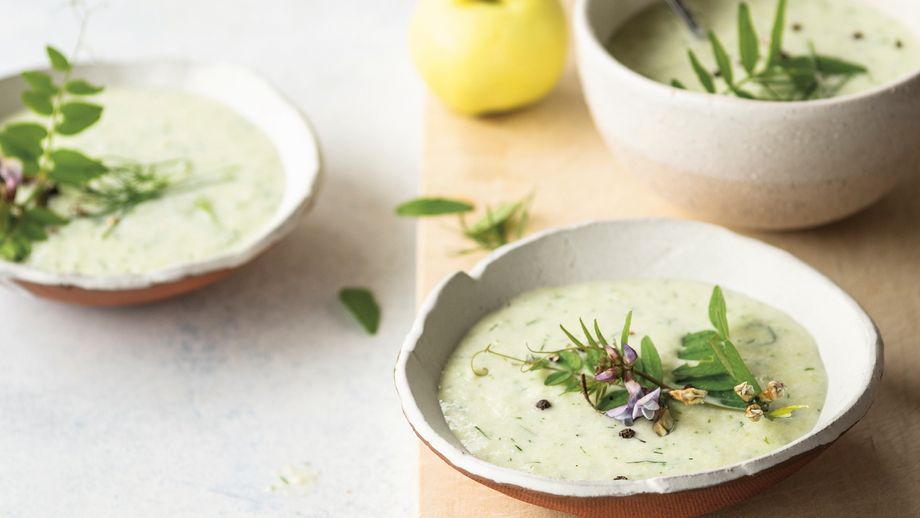 Holzbrett, Löffel und zwei Schalen mit grüner Suppe mit frischen Kräutern dekoriert